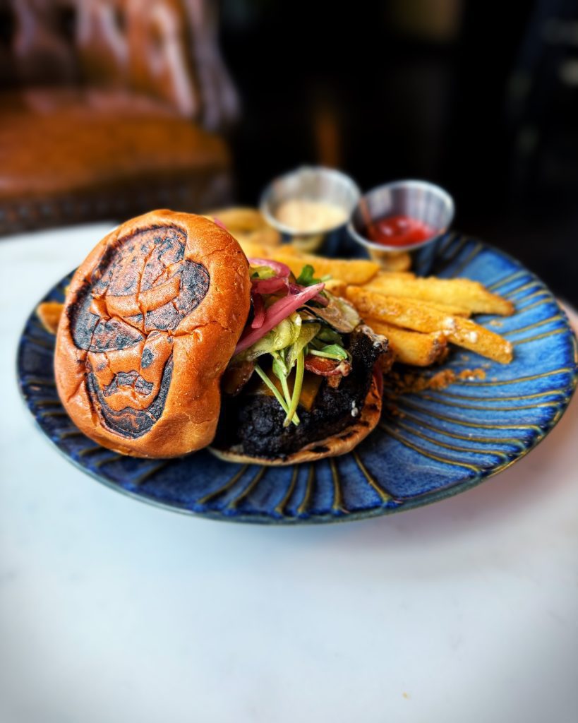 The 1921 Burger at Lefty’s on the Square in Magnolia, Arkansas — Lefty’s silhouette branded into the top bun, served on a blue ceramic plate with double-battered fries and house secret sauce.